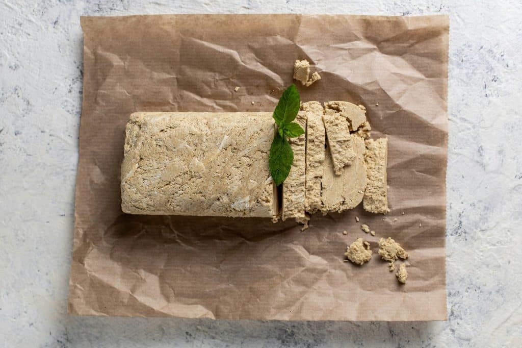 Cutted halva on craft paper. Sweet dessert with mint on white background